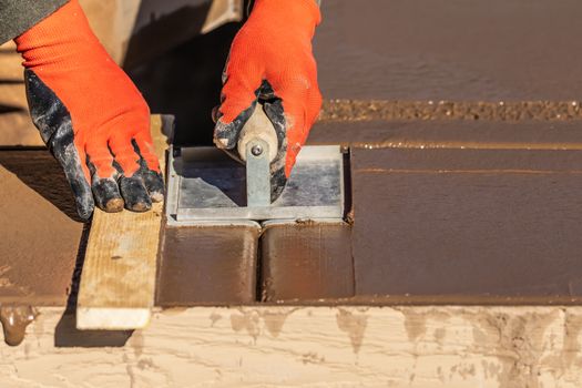 Construction Worker Using Hand Groover On Wet Cement Forming Coping Around New Pool.