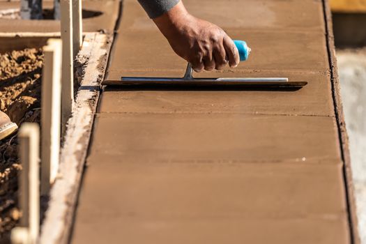 Construction Worker Using Trowel On Wet Cement Forming Coping Around New Pool.