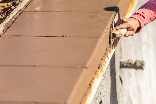 Construction Worker Using Wood Trowel On Wet Cement Forming Coping Around New Pool.