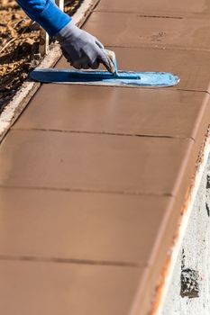 Construction Worker Using Trowel On Wet Cement Forming Coping Around New Pool.