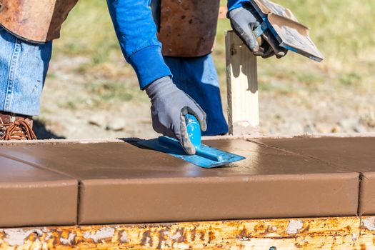 Construction Worker Using Trowel On Wet Cement Forming Coping Around New Pool.