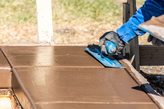 Construction Worker Using Trowel On Wet Cement Forming Coping Around New Pool.