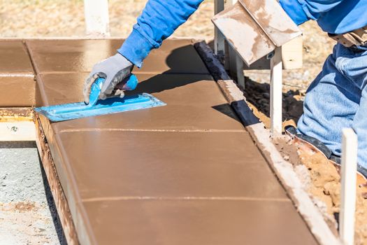 Construction Worker Using Trowel On Wet Cement Forming Coping Around New Pool.