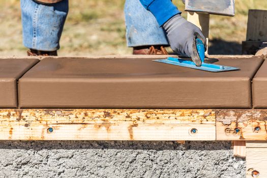 Construction Worker Using Trowel On Wet Cement Forming Coping Around New Pool.