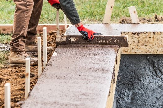 Construction Worker Leveling Wet Cement Into Wood Framing.