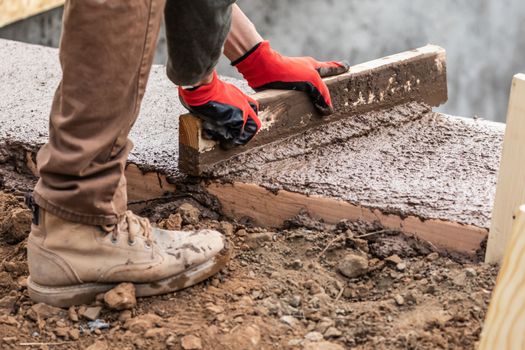 Construction Worker Leveling Wet Cement Into Wood Framing.