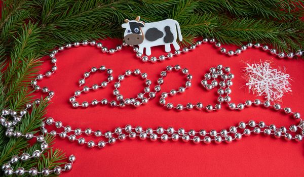 Spruce branches ,a white bull on a red background and the numbers 2021 ,lined with silver beads. The concept of a New year.
