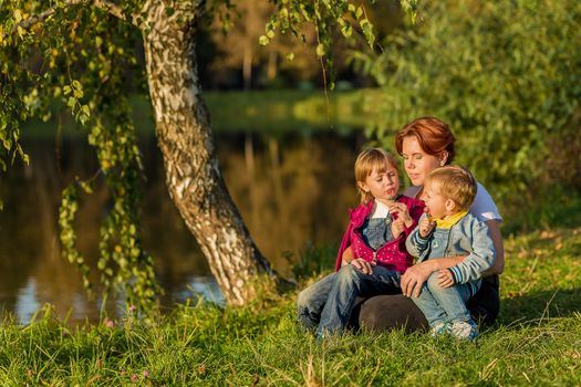 Mom and children sit on the river bank in the rays of the setting sun on an autumn evening