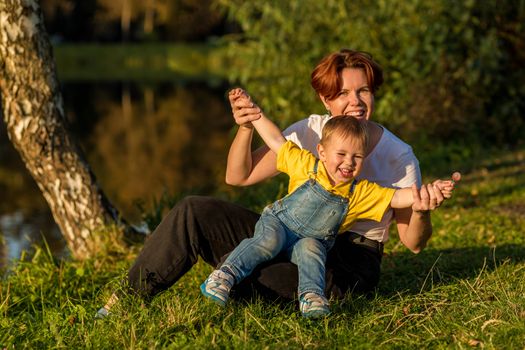 Mom and little boy sit on the river bank in the rays of the setting sun on an autumn evening