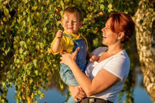 Mom and little boy sit on the river bank in the rays of the setting sun on an autumn evening