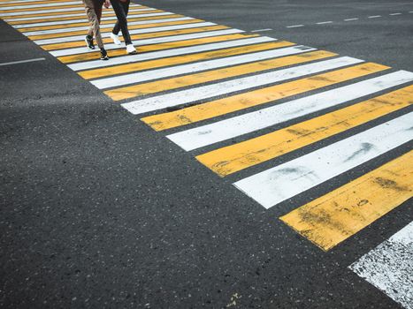 Two young man cross the road at a pedestrian crossing. White and yellow stripes on asphalt - zebra crossing. Traffic sign. City road marking.