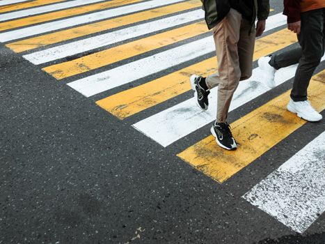 Two young man cross the road at a pedestrian crossing. White and yellow stripes on asphalt - zebra crossing. Traffic sign. City road marking.