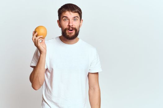 a man with an orange in a white t-shirt on a light background the diet of a brunette thick beard. High quality photo
