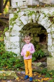 A girl with a broken arm stands near a brick wall in an old park on an autumn walk