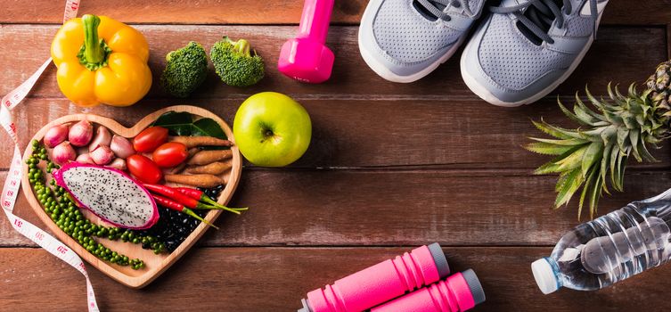 Top view of various fresh organic fruit and vegetable in heart plate and sports shoes, dumbbell and water, studio shot on wooden gym table, Healthy diet vegetarian food concept, World food day