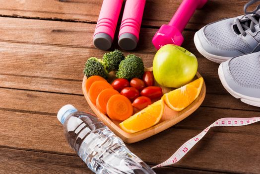 Top view of fresh fruits and vegetables in heart plate wood (apple, carrot, tomato, orange, broccoli) and dumbbells, sport shoes sports equipment on wooden table, Healthy lifestyle diet food concept