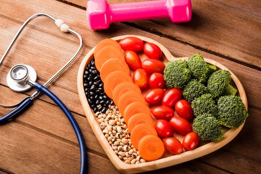 Top view of fresh organic fruits and vegetables in heart plate wood (carrot, Broccoli, tomato), doctor stethoscope and sport dumbbell on wooden table, Healthy lifestyle diet food concept