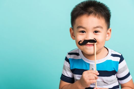 Funny happy hipster kid holding black mustache props for the photo booth close face, studio shot isolated on a blue background, Men health awareness, Prostate Cancer Awareness