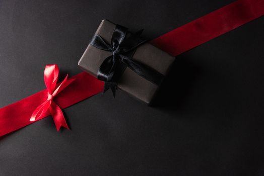 Black Friday Sale concept, Top view of gift box wrapped black paper and black bow ribbon press, studio shot on and having red ribbon across a dark background