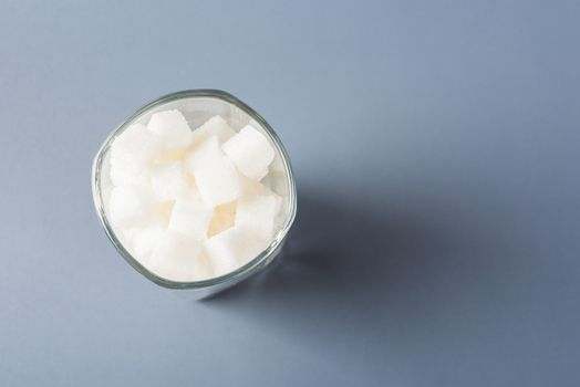 Top view glass full of white sugar cube sweet food ingredient, studio shot isolated on gray background, health high blood risk of diabetes and calorie intake concept and unhealthy drink