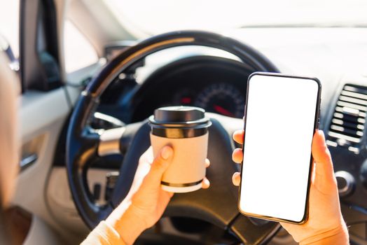 Asian woman drinking hot coffee takeaway cup inside a car and using smartphone blank screen while driving the car in the morning during going to work on highway, Transportation and vehicle concept