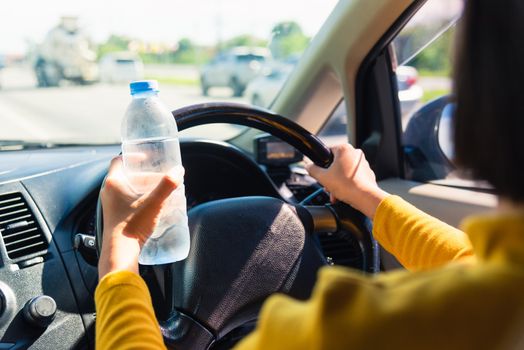 Asian woman holding a water bottle for drink while driving the car in the morning during going to work on highway road, Transportation and vehicle concept