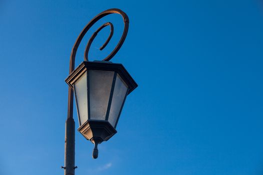Low-angle view of antique style lampposts against a bright blue sky.