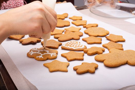 Close up of hand decorating the gingerbread cookies with white glaze, Merry Christmas concept