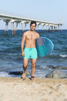 Young attractive surfer holding his surfboard at the beach