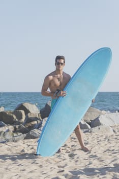 Young attractive surfer holding his surfboard at the beach