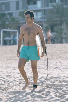 Young attractive surfer holding his surfboard at the beach