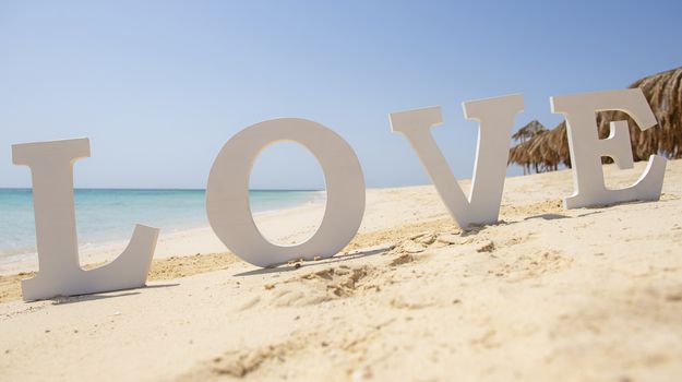 Closeup of romantic love sign on tropical island sandy beach paradise with ocean in background