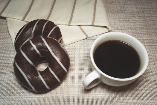 Coffee in a white cup and chocolate donuts, top view