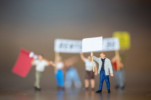 Miniature people , Crowd of protesters people raised hands and shouting on wooden background.