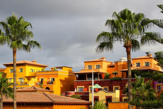 View on Playa de Las Americas on canary island tenerife with plam trees, orange colored  houses and dark clouds