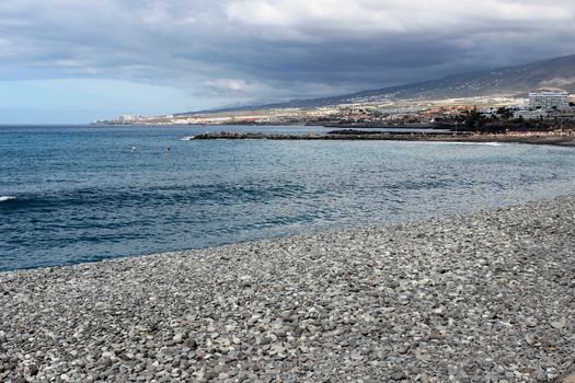 Stony beach at Playa de Las Americas on canary island tenerife with blue water and blue sky