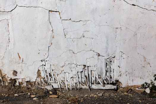 poor wattle and daub cracked stucco wall with white plaster and ground line
