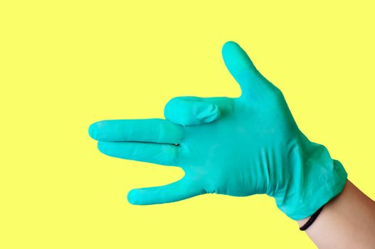 Female hand in blue latex glove makes a gesture resembling a dog with open mouth isolate a light yellow background. Medical health concept.