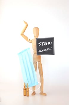 World epidemic of coronavirus. wooden man is isolated on a white background holds a medical protective mask and a sign that says: stop, pandemic. Outbreak Defense Concept. Copy Space.