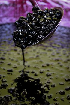 Chokeberry berries in a ladle above a pot full of chokeberry jam. Zavidovici, Bosnia and Herzegovina.