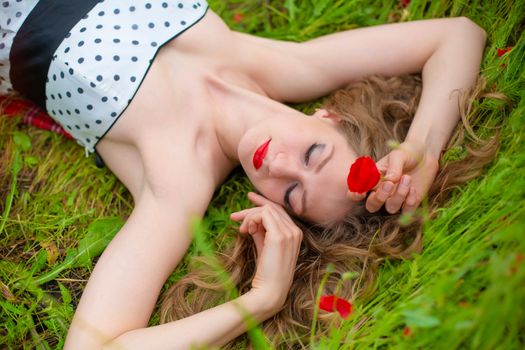 A young long-haired girl enjoys the colors of nature on a blooming poppy field on a hot summer day.