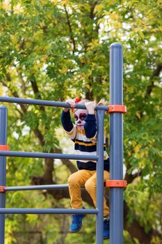 A little preschool girl with Painted Face, climbed the Swedish wall in the playground, celebrates Halloween or Mexican Day of the Dead.