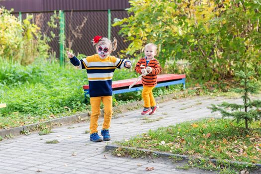 A little preschool girl with Painted Face, running away from brother in the playground, celebrates Halloween or Mexican Day of the Dead.