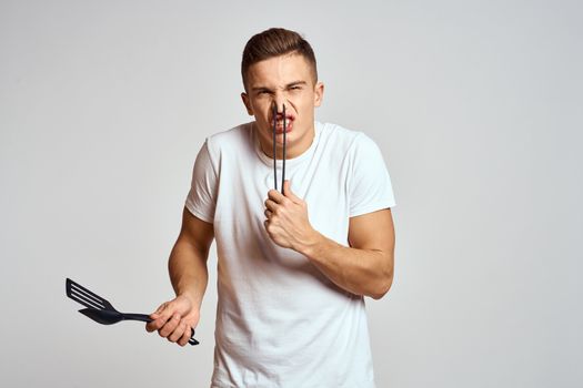 Guy with kitchen tools in hands on a light background cropped view of emotions fun model. High quality photo