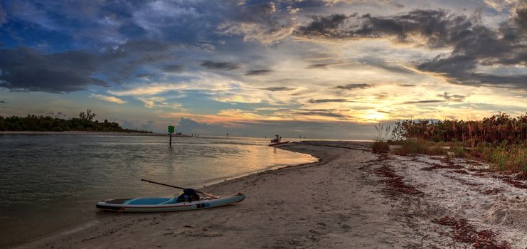 Paddleboard on white sand at sunset as clouds hang over Barefoot Beach in Bonita Springs, Florida.