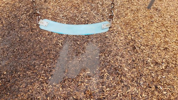 blue swing seat with water puddle on mulch or wood chips