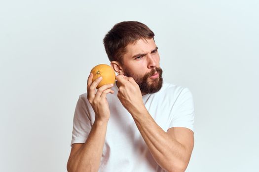 a man with an orange in a white t-shirt on a light background the diet of a brunette thick beard. High quality photo