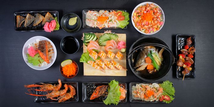 Traditional Japanese food - salmon salad sushi, rolls, rice with shrimp and sauce on a dark background. Top view