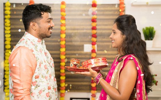 Woman in traditional dress doing Karwa Chauth ritual or celebration with partner or Husband at home - Karwa Chauth is festival of happiness and togetherness celebrated in India