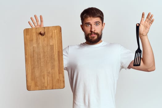 Man with a kitchen wooden board and with a shovel on a light background emotions white t-shirt model. High quality photo